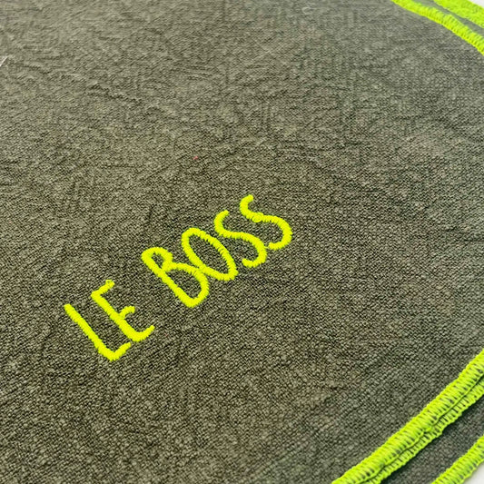 Serviette en lin lavé couleur vert safari, finition jaune néon, avec un nom brodé. Vue du détail de la broderie du produit