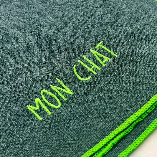 Serviette en lin lavé couleur vert forêt, finition vert néon, avec un nom brodé. Vue du détail de la broderie du produit