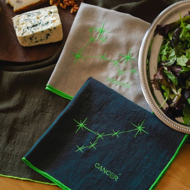 Serviettes verte et grise en lin brodées de constellations d'étoiles, représentant les signes astrologiques.