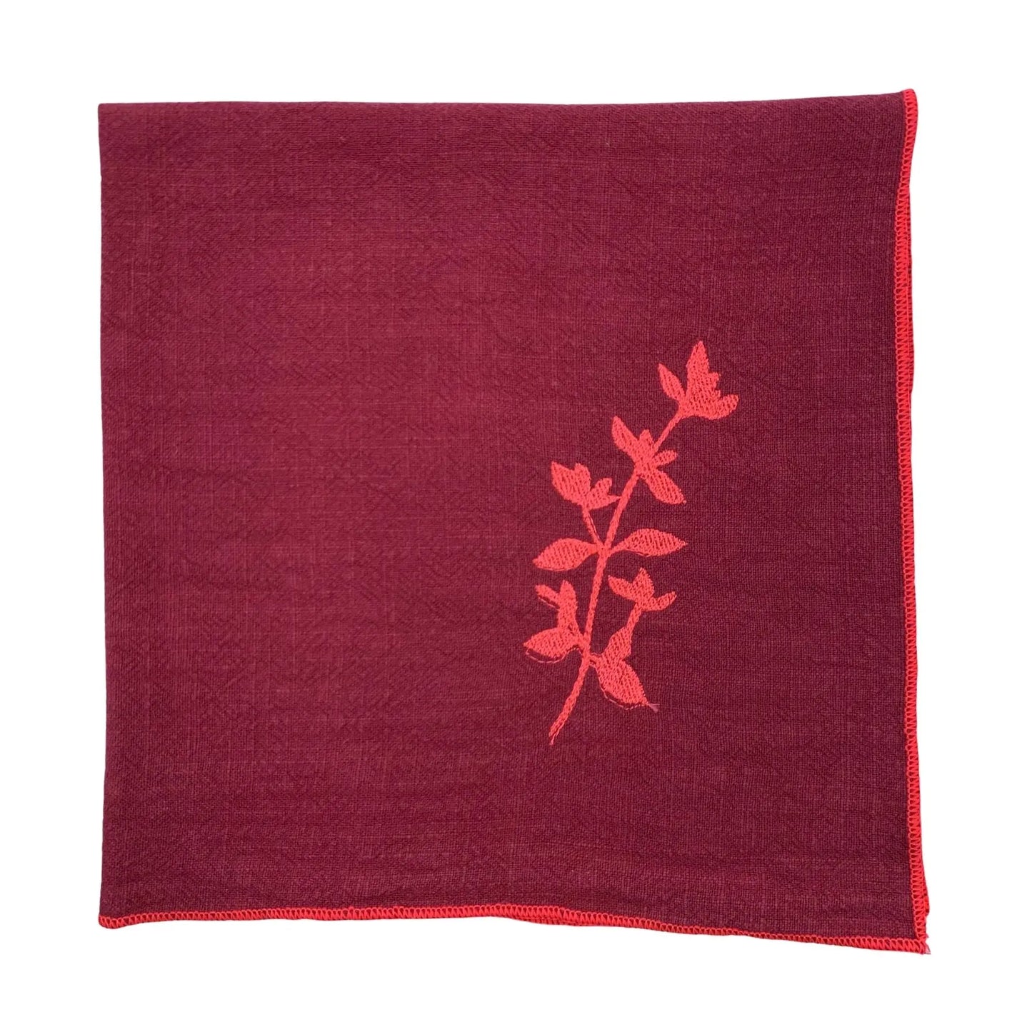 Serviette de table en lin lavé de couleur framboise, ornée de finitions en rose néon. Elle présente un motif brodé de thym, une plante aromatique. Vue du produit.
