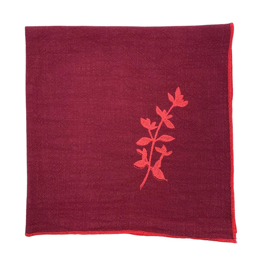 Serviette de table en lin lavé de couleur framboise, ornée de finitions en rose néon. Elle présente un motif brodé de thym, une plante aromatique. Vue du produit.