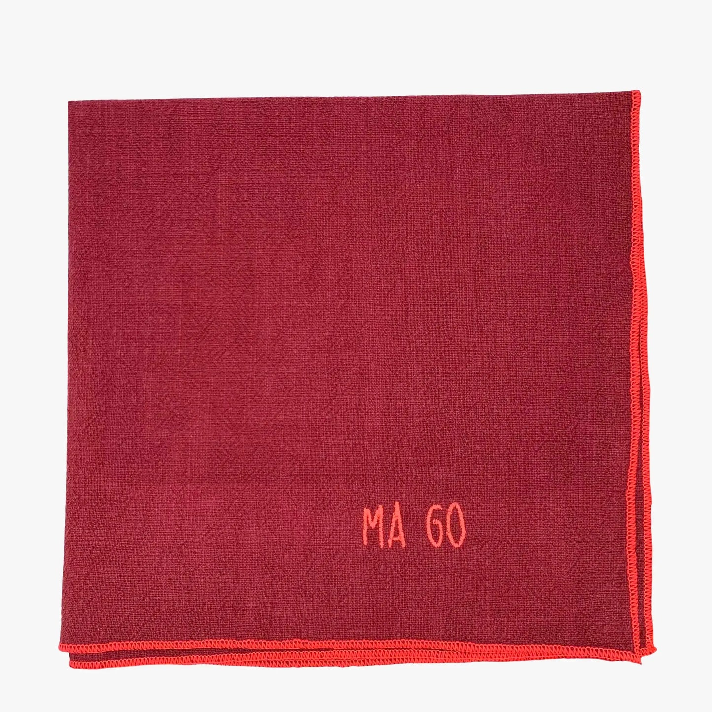 Serviette en lin lavé couleur framboise, finition rose néon, avec un nom brodé. Vue du produit