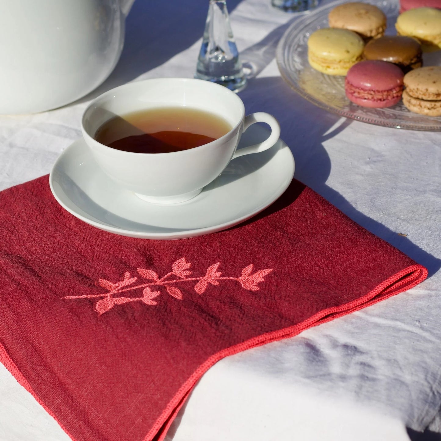 Serviette de table en lin lavé de couleur framboise, ornée de finitions en rose néon. Elle présente un motif brodé de thym, une plante aromatique. Vue du produit.
