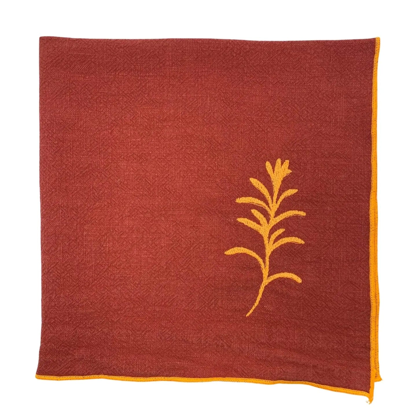 Serviette de table en lin lavé de couleur piment, ornée de finitions en orange néon. Elle présente un motif brodé de romarin, une plante aromatique. Vue du produit.