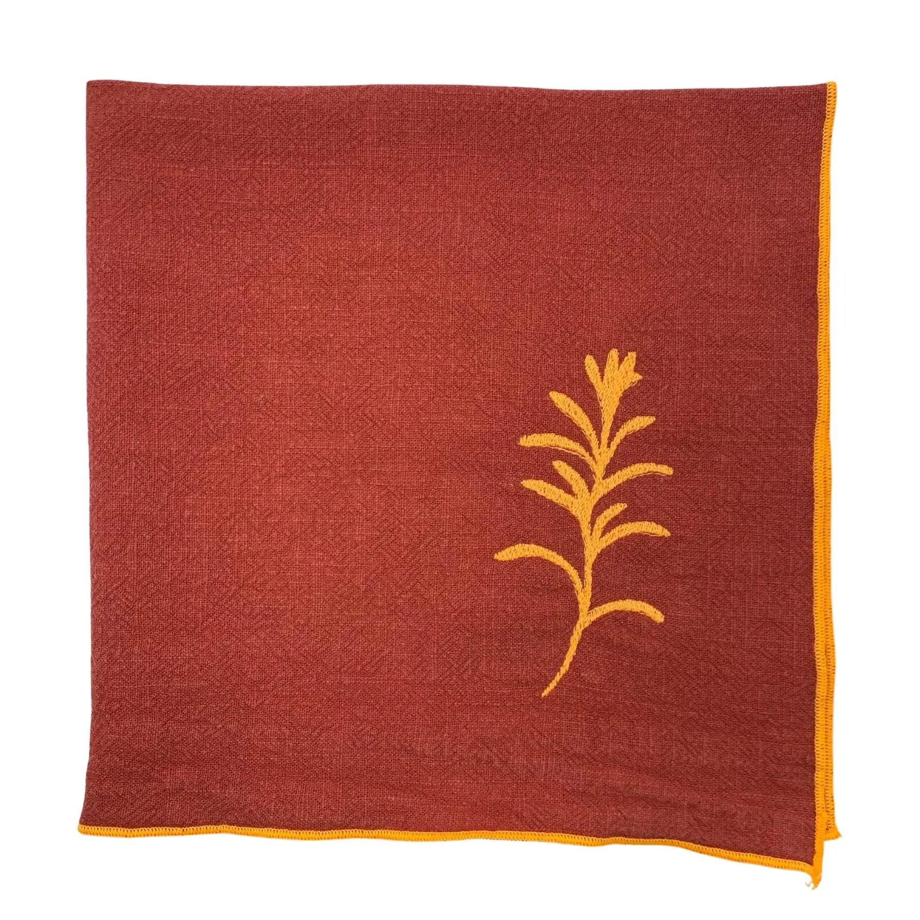 Serviette de table en lin lavé de couleur piment, ornée de finitions en orange néon. Elle présente un motif brodé de romarin, une plante aromatique. Vue du produit.