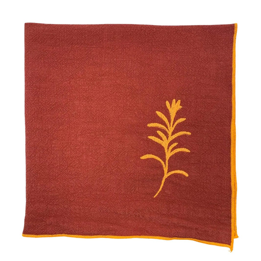 Serviette de table en lin lavé de couleur piment, ornée de finitions en orange néon. Elle présente un motif brodé de romarin, une plante aromatique. Vue du produit.