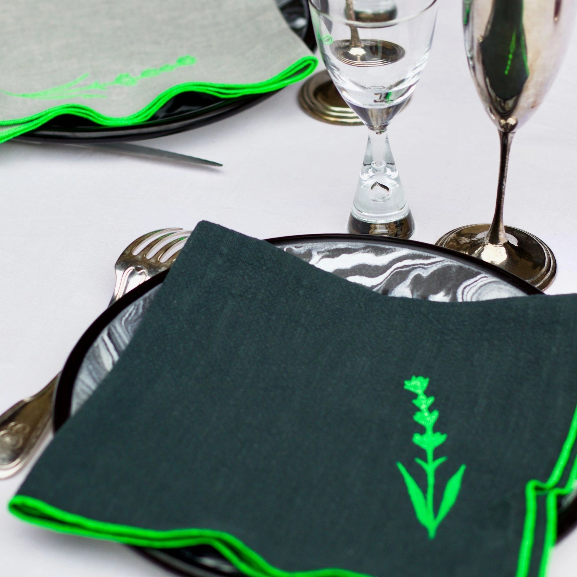 Serviette de table en lin de couleur grise, ornée de finitions en vert néon. Elle présente un motif brodé de lavande, une plante aromatique. Vue du produit en situation.