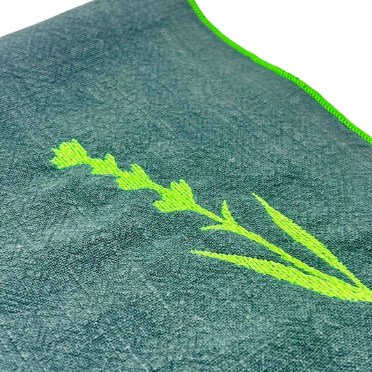 Serviette de table en lin lavé de couleur vert forêt, avec des finitions en vert néon. Elle est brodée d'un motif de lavande, une plante aromatique. Vue du détail de la broderie