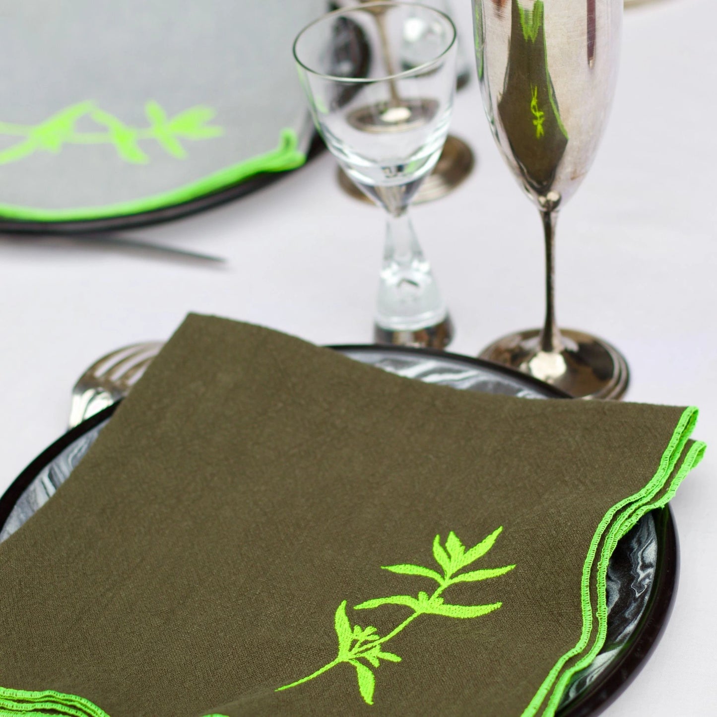 Serviette de table en lin de couleur grise, ornée de finitions en jaune néon. Elle présente un motif brodé de sarriette, une plante aromatique. Vue du produit en situation.