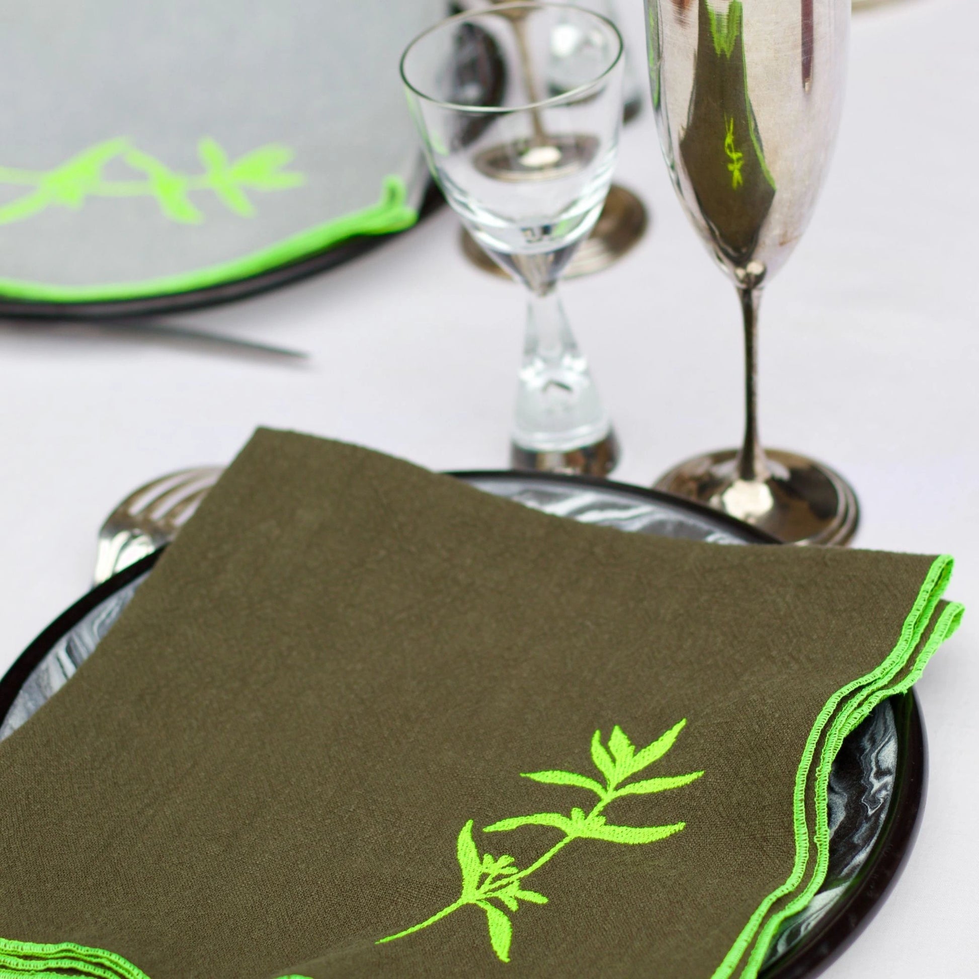 Serviette de table en lin de couleur grise, ornée de finitions en jaune néon. Elle présente un motif brodé de sarriette, une plante aromatique. Vue du produit en situation.