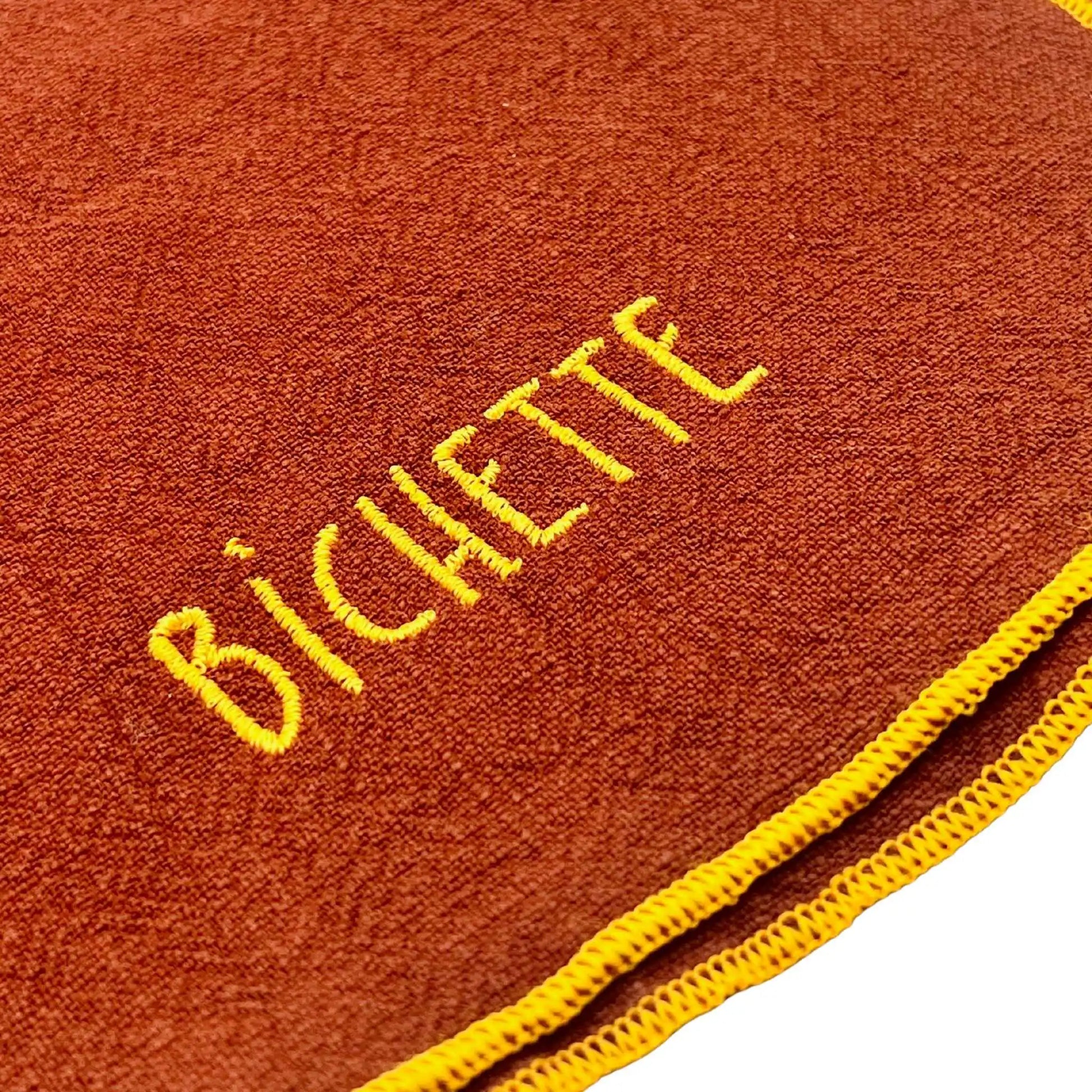 Serviette en lin lavé couleur piment finition orange néon, avec un nom brodé. Vue du détail de la broderie du produit